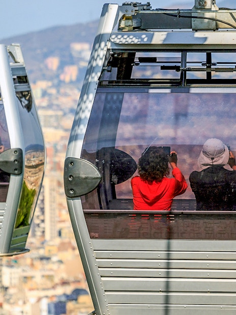 Montjuic cable cars with passengers overlooking Barcelona cityscape.