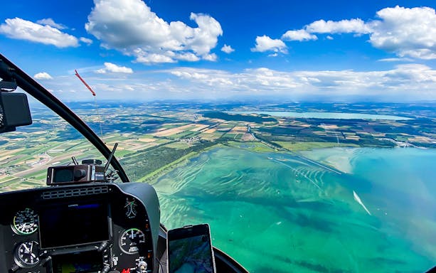 Helicopter cockpit view over Bernese Seeland and Jura landscape.