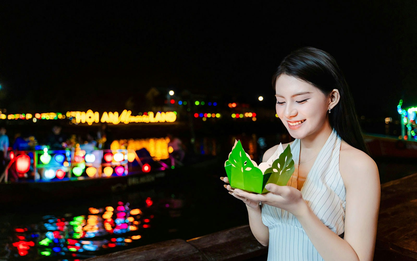 Girl holding paper lantern by Hoi An river at night.