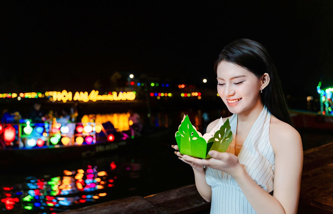Girl holding paper lantern by Hoi An river at night.