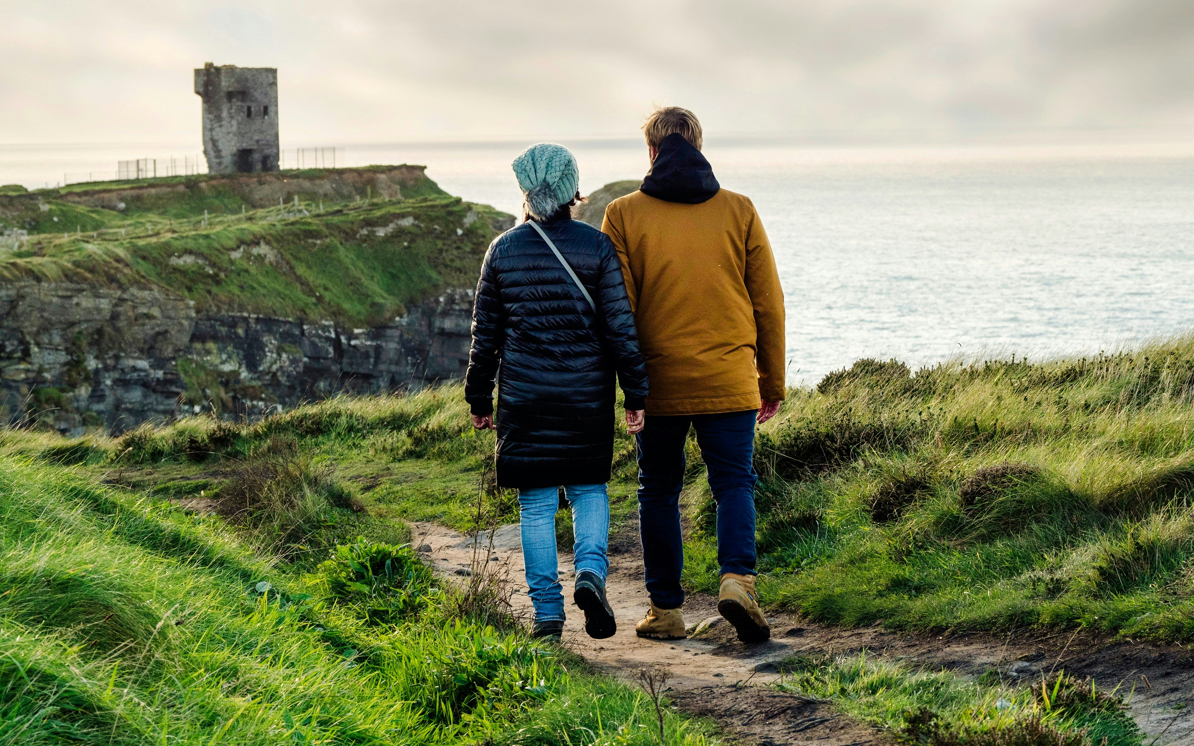 Couple walking towards Moher Tower at Hag's Head, Ireland, along a coastal path.