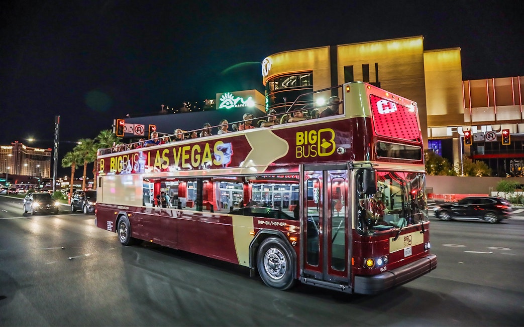 Big Bus tour in Las Vegas at night with passengers on upper deck.