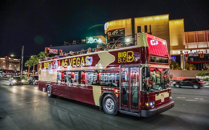 Big Bus tour in Las Vegas at night with passengers on upper deck.