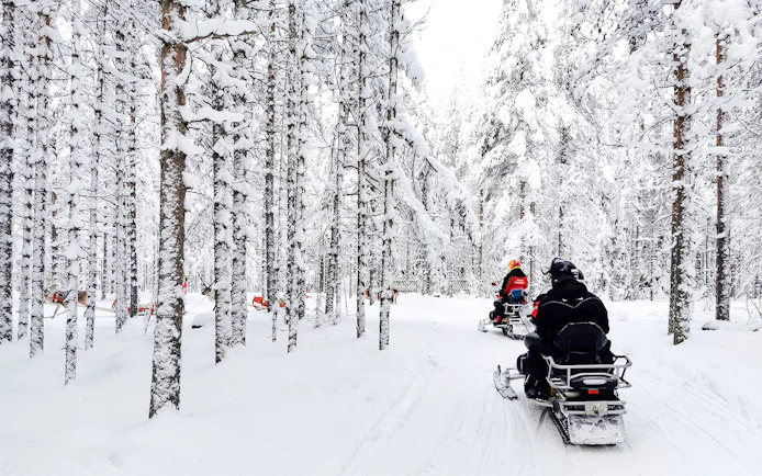 Snowmobile riders in snowy forest, Rovaniemi tour.