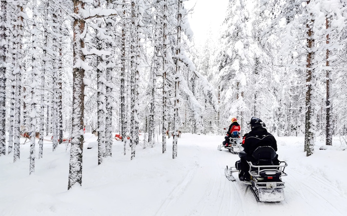 Snowmobile riders in snowy forest, Rovaniemi tour.
