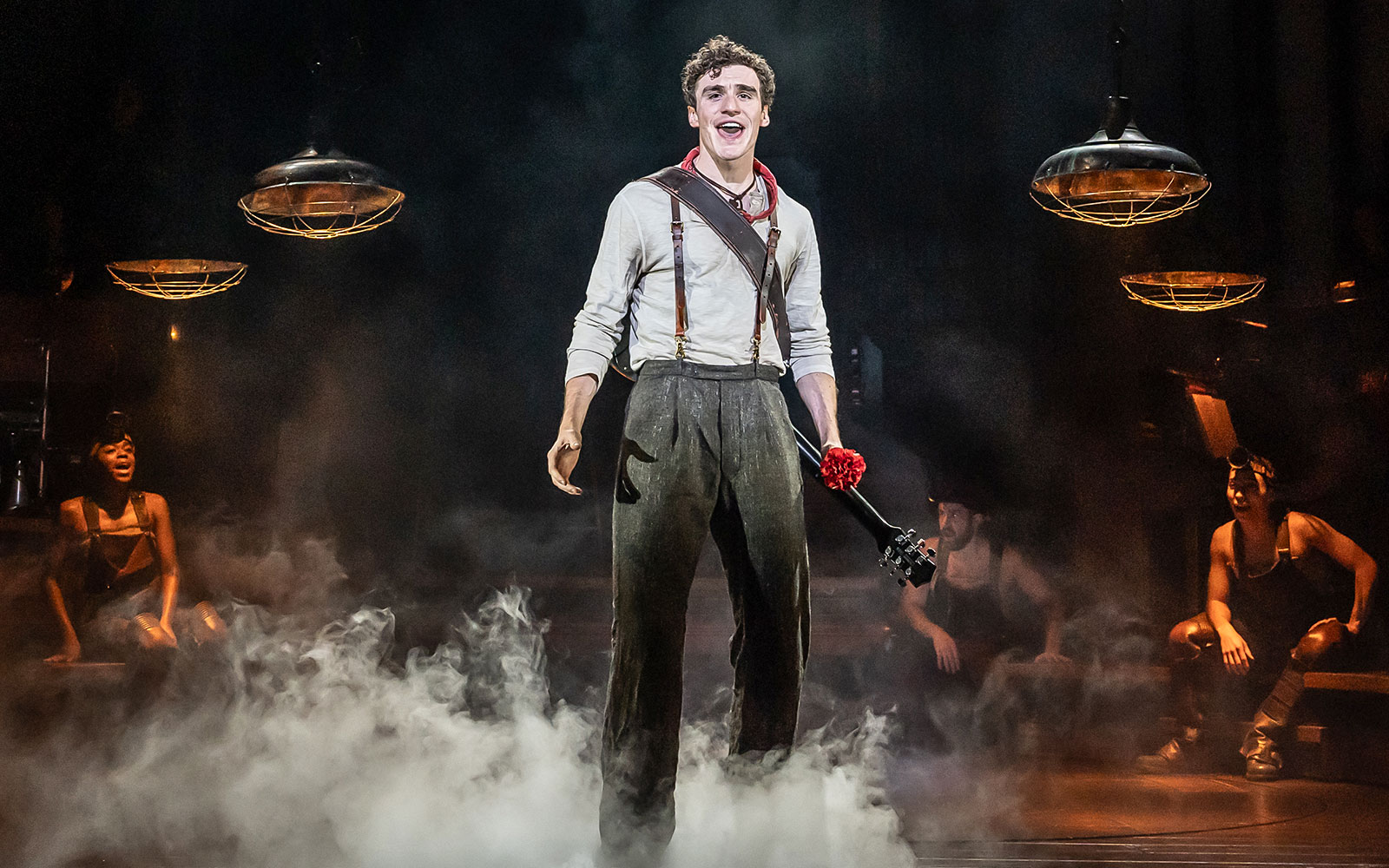Performer on stage during Hadestown musical with guitar and red flower.