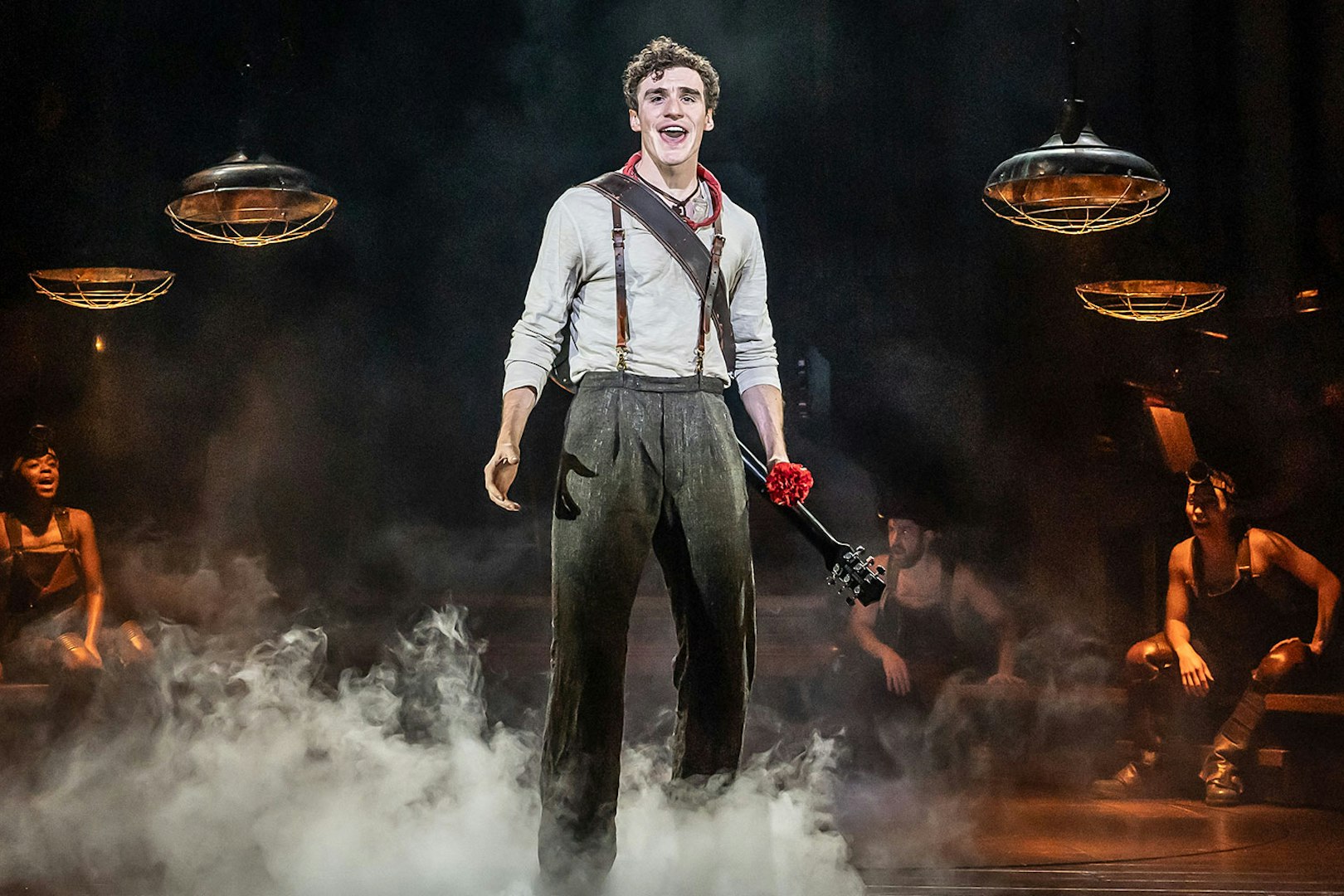 Performer on stage during Hadestown musical with guitar and red flower.