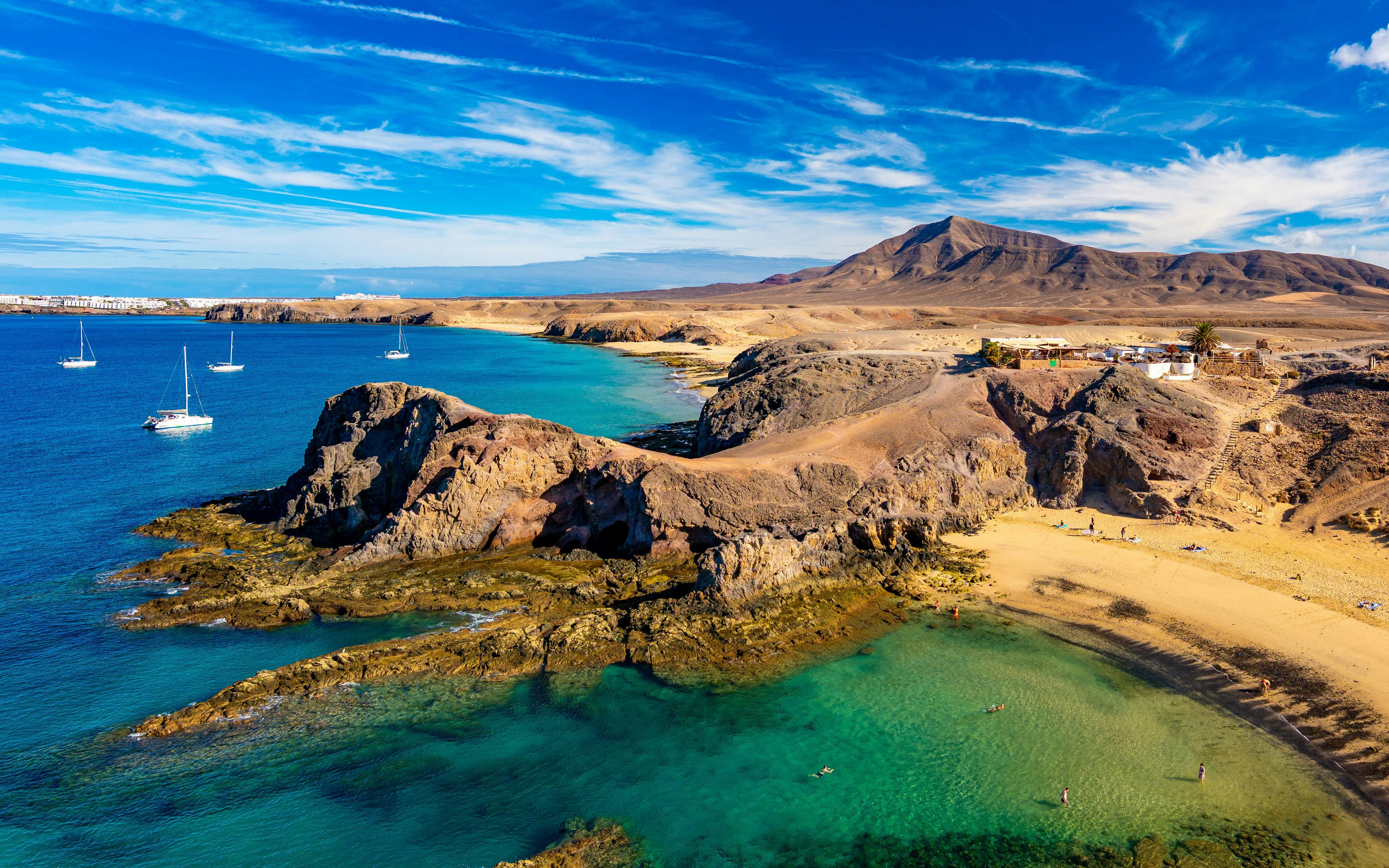 Sailboats near rocky coastline at Playa de Papagayo, Lanzarote.