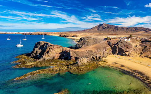 Sailboats near rocky coastline at Playa de Papagayo, Lanzarote.