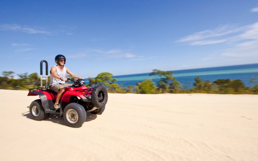 Man driving red quad bike on sandy track with ocean view on Moreton Island.