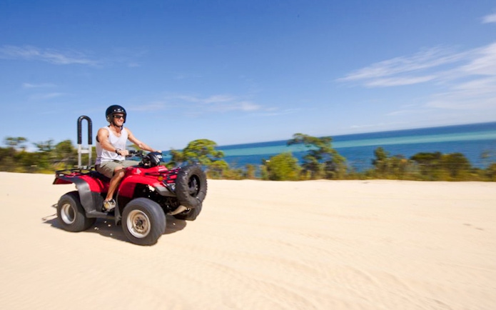 Man driving red quad bike on sandy track with ocean view on Moreton Island.
