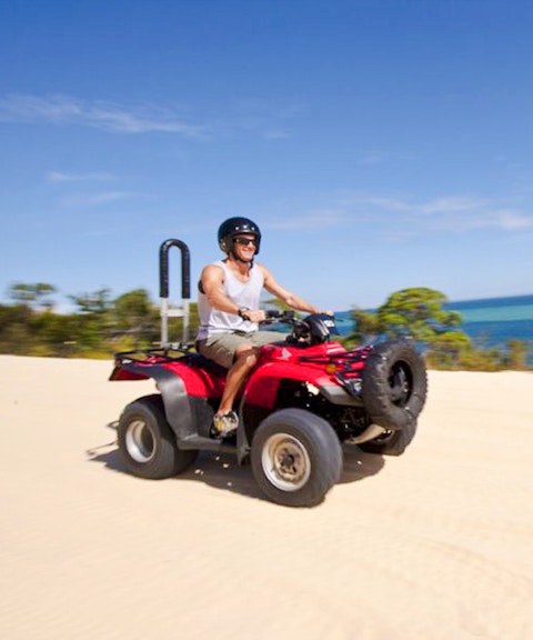 Man driving red quad bike on sandy track with ocean view on Moreton Island.