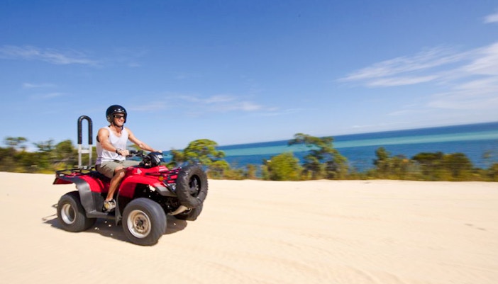 Man driving red quad bike on sandy track with ocean view on Moreton Island.