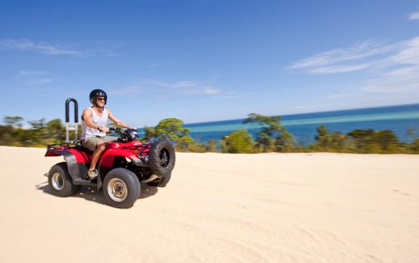 Man driving red quad bike on sandy track with ocean view on Moreton Island.