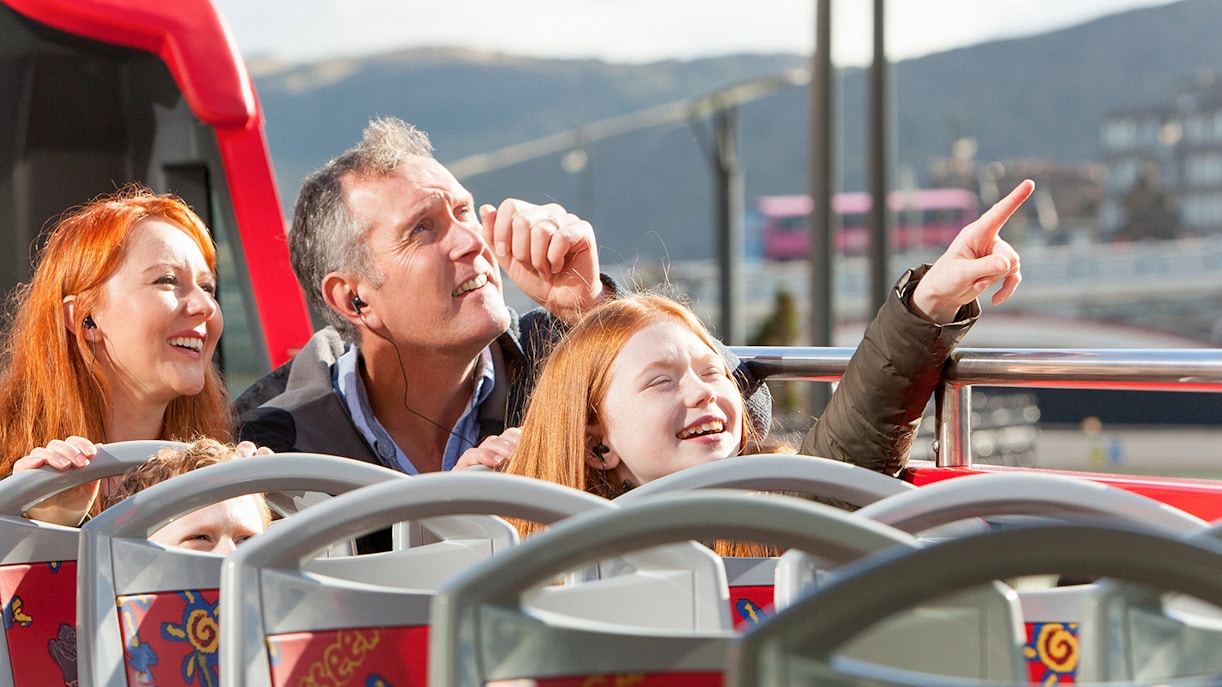 A family of three people enjoying the views from the hop on hop off bus tour while listening to the audioguide