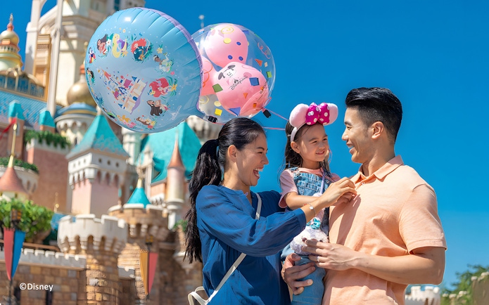 Family enjoying balloons at Hong Kong Disneyland with castle in background.