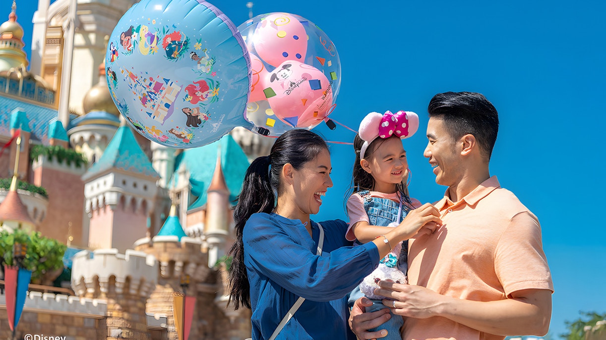 Family enjoying balloons at Hong Kong Disneyland with castle in background.