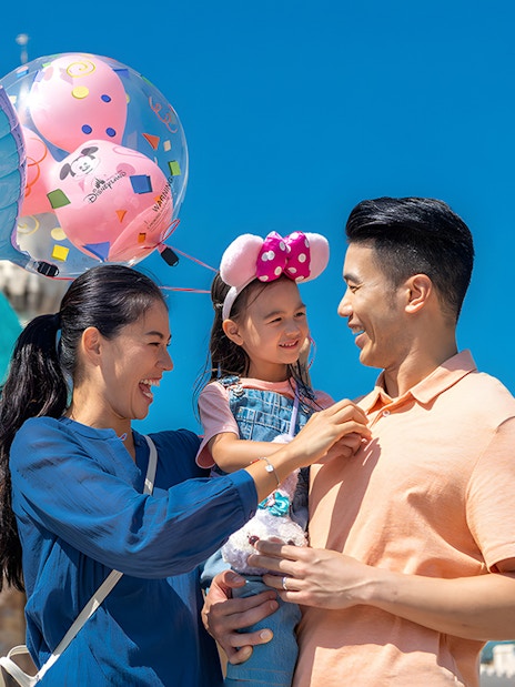 Family enjoying balloons at Hong Kong Disneyland with castle in background.