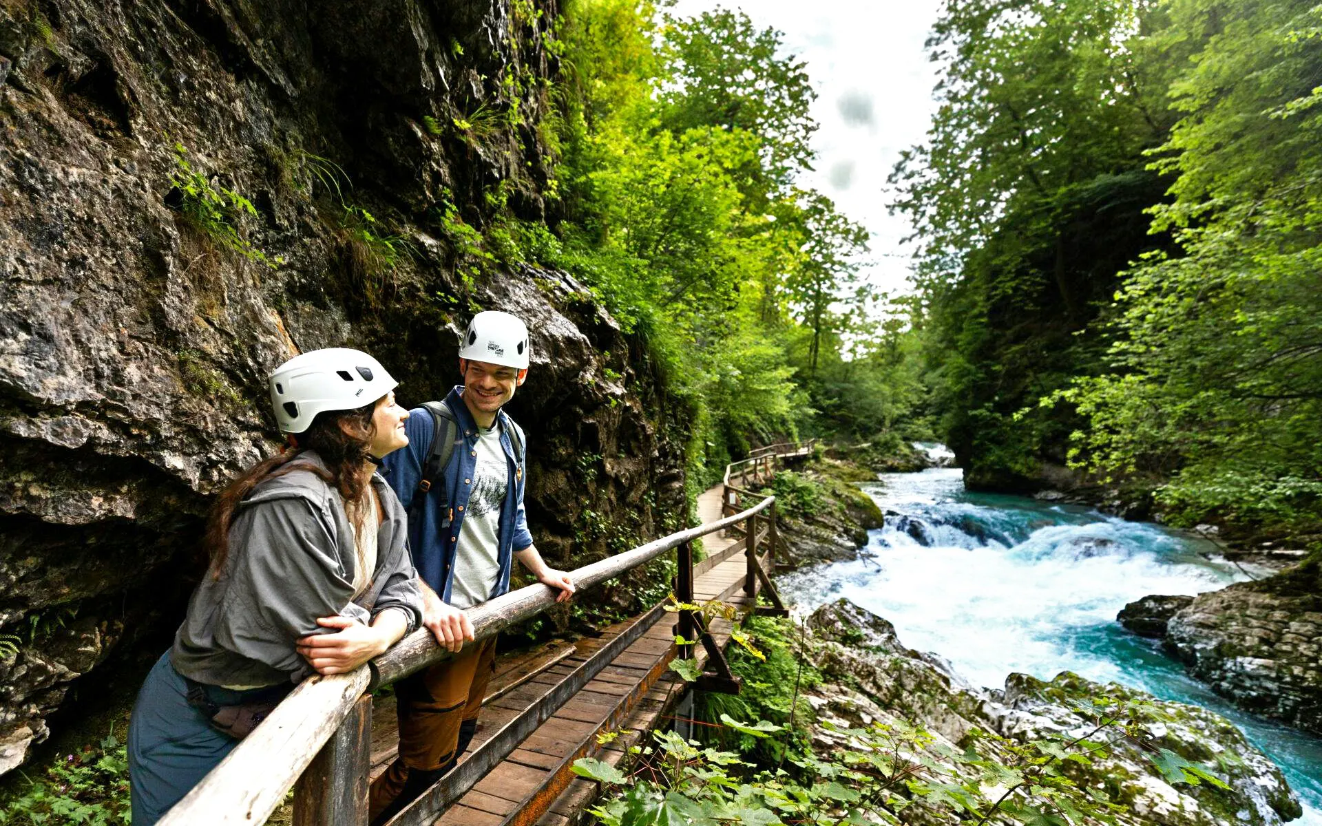 Couple walking along wooden path at Vintgar Gorge, Slovenia, near a flowing river.