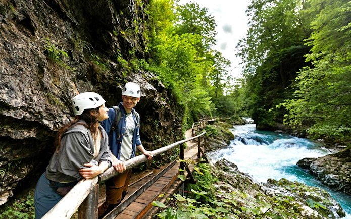 Couple walking along wooden path at Vintgar Gorge, Slovenia, near a flowing river.