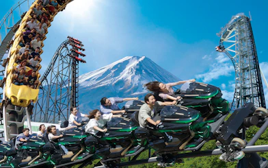 People enjoying a rollercoaster ride at Fuji-Q Highland with Mount Fuji in the background.