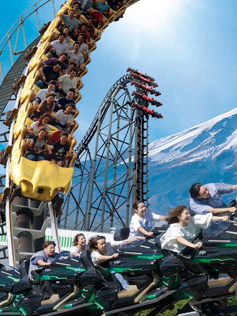 People enjoying a rollercoaster ride at Fuji-Q Highland with Mount Fuji in the background.