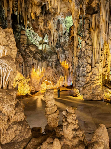 Stalactites and stalagmites in Nerja Cave, Spain, with a visitor exploring the formations.