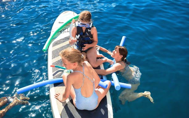 Guests swimming and paddleboarding on Premium Catamaran Day Cruise from Souda to Marathi Bay.