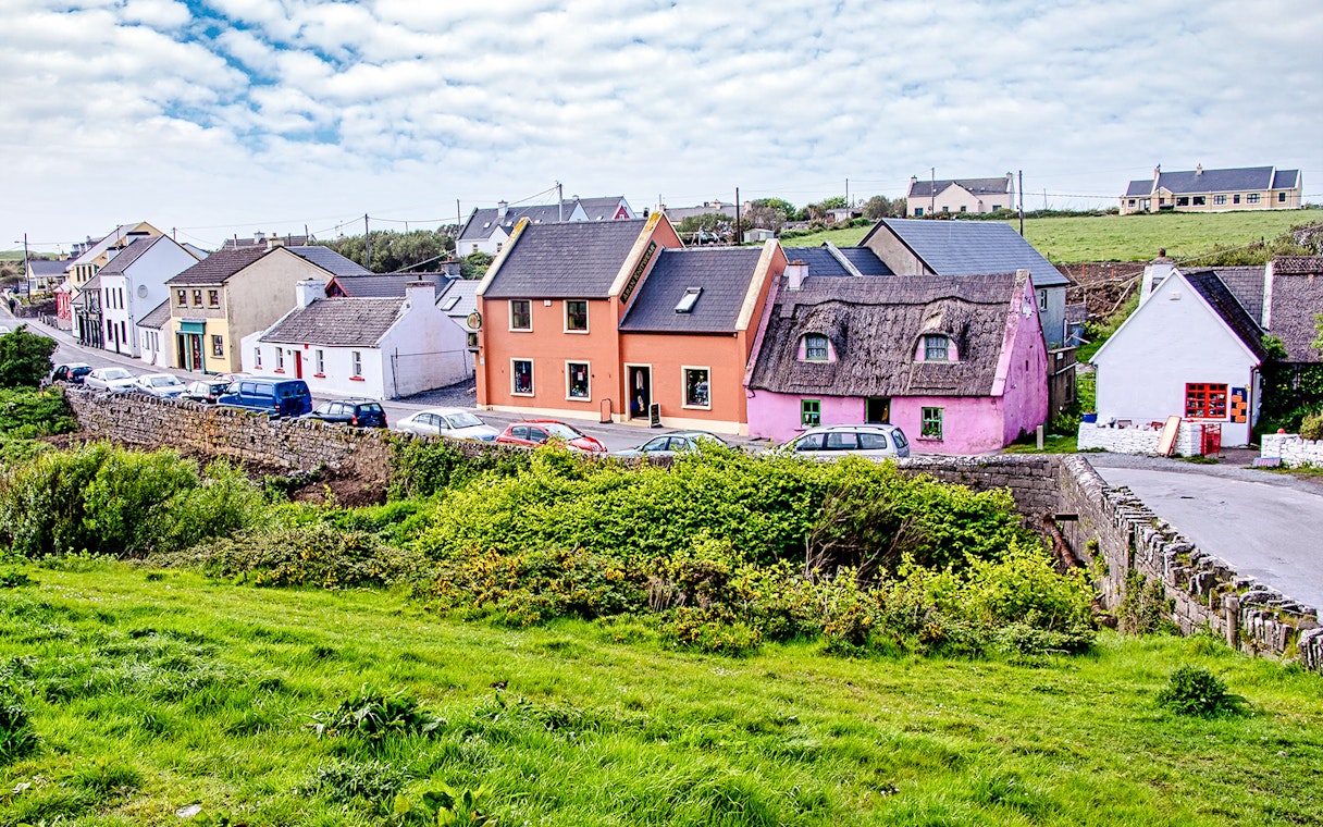 Colorful houses along a street in Doolin Village, Ireland, with lush greenery in the foreground.