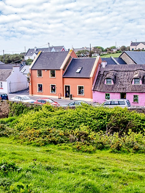 Colorful houses along a street in Doolin Village, Ireland, with lush greenery in the foreground.