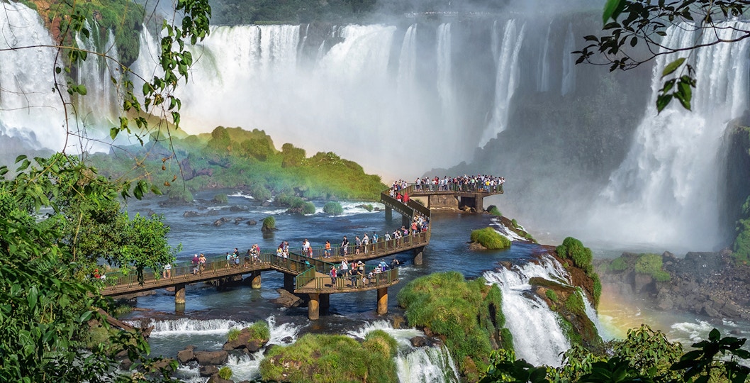 Tourists exploring Iguazu Falls, Argentina, with cascading waterfalls in the background.