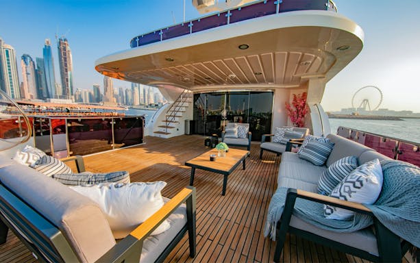 Super-yacht deck with seating, Dubai Marina skyline and Ferris wheel in the background.