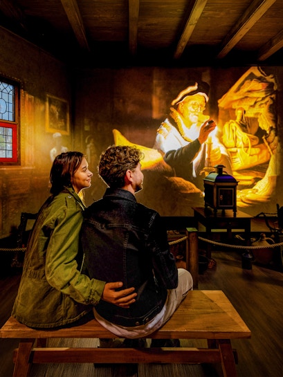 Couple watching Rembrandt projection at Amsterdam museum exhibit.