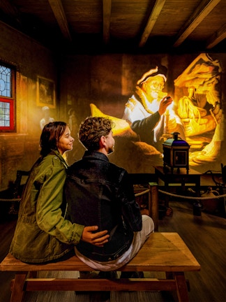 Couple watching Rembrandt projection at Amsterdam museum exhibit.