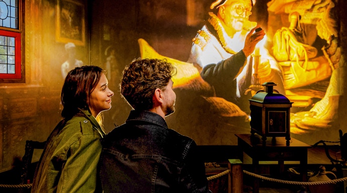 Couple watching Rembrandt projection at Amsterdam museum exhibit.