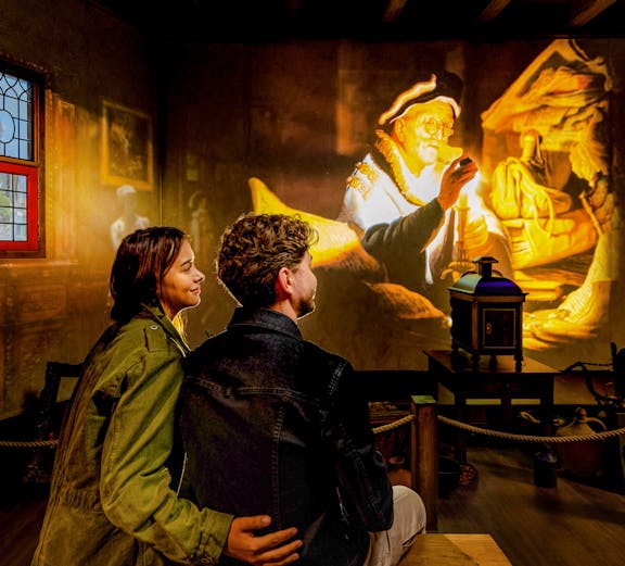 Couple watching Rembrandt projection at Amsterdam museum exhibit.