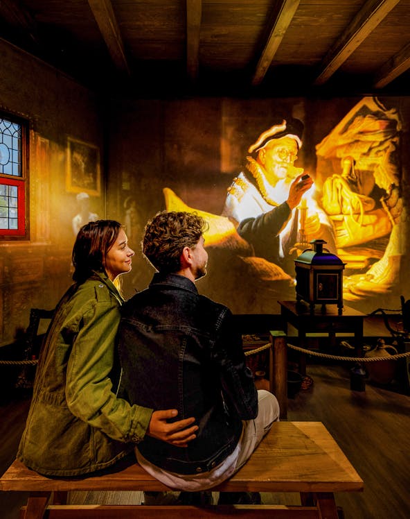 Couple watching Rembrandt projection at Amsterdam museum exhibit.