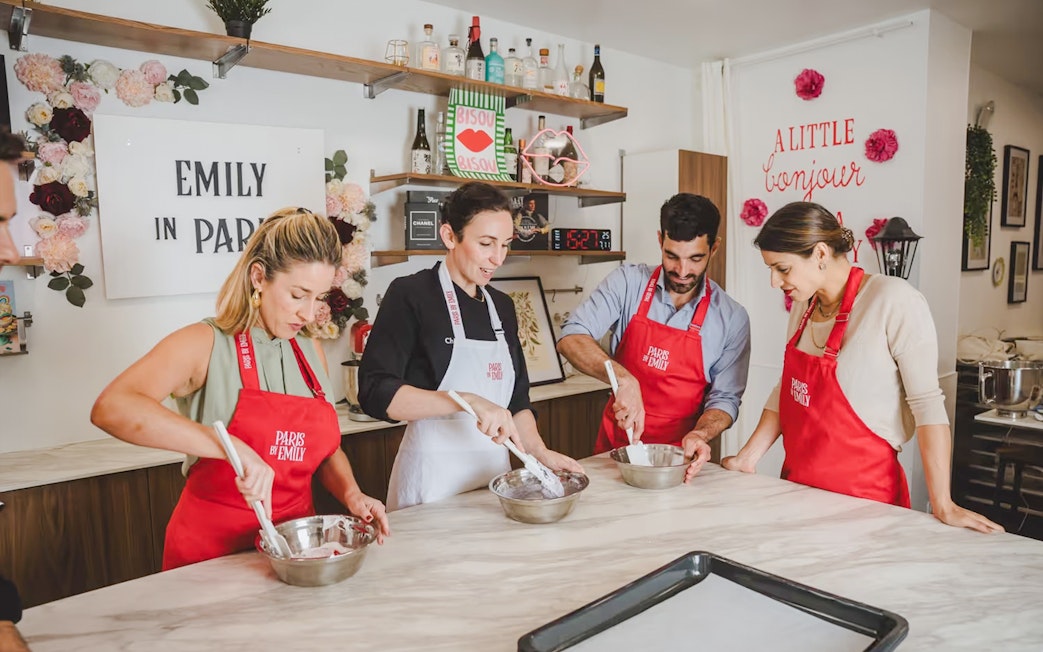 Participants in a macaron-making workshop in Paris, wearing red aprons and mixing ingredients.