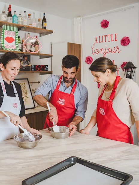 Participants in a macaron-making workshop in Paris, wearing red aprons and mixing ingredients.
