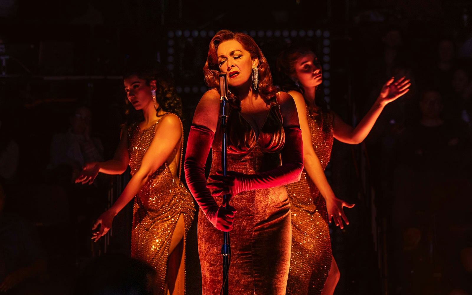 Singer performing on stage with backup dancers in a dimly lit theater.