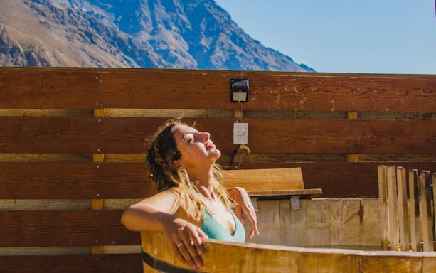 Tourist relaxing in a wooden hot tub at Lodge El Morado with mountain view.