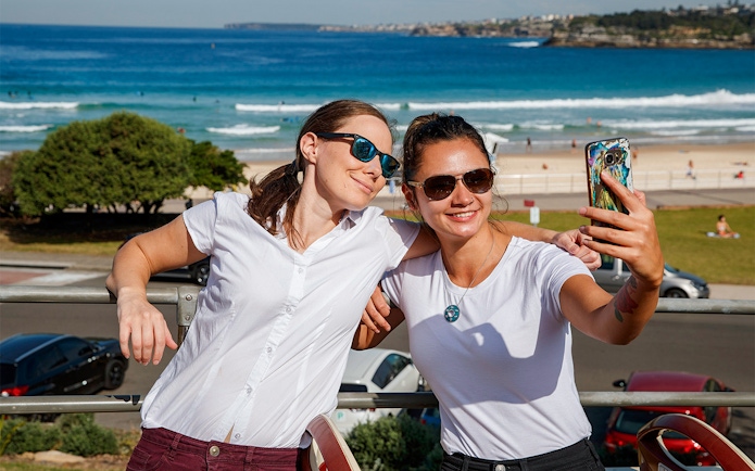 Passengers taking a selfie on Big Bus Sydney with Bondi Beach in the background.