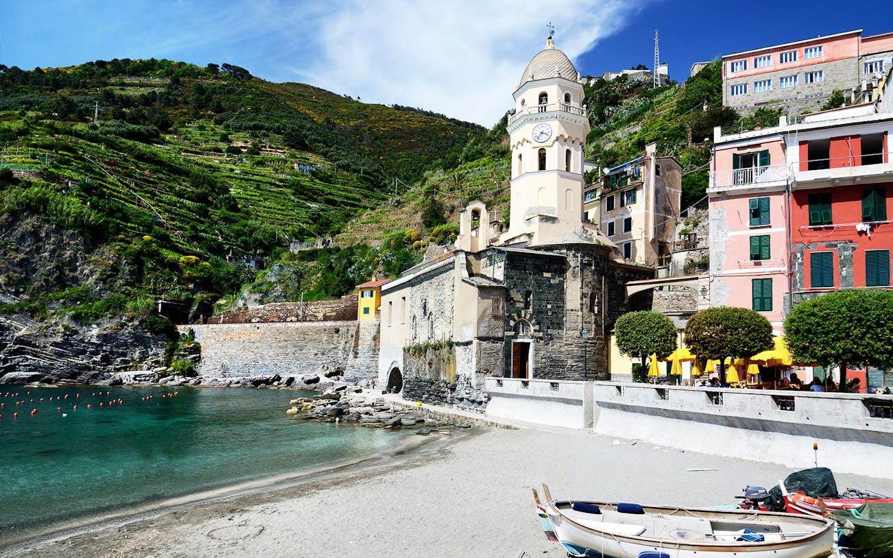 Cinque Terre coastal village with colorful buildings and church tower, viewed from the beach.