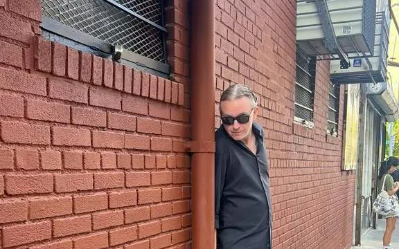 Man in sunglasses leaning against a brick wall on New York's Lower East Side during a murder mystery game.
