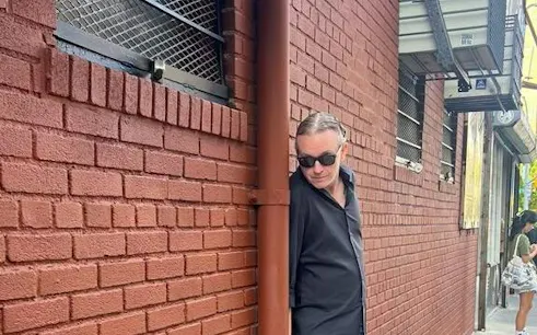 Man in sunglasses leaning against a brick wall on New York's Lower East Side during a murder mystery game.