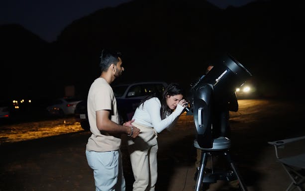 Visitors using a telescope at Mleiha Space Camp during a nighttime stargazing session.