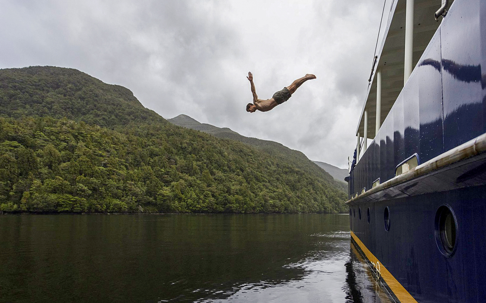 Person diving from a boat into Doubtful Sound, surrounded by lush hills, during an overnight cruise from Te Anau.