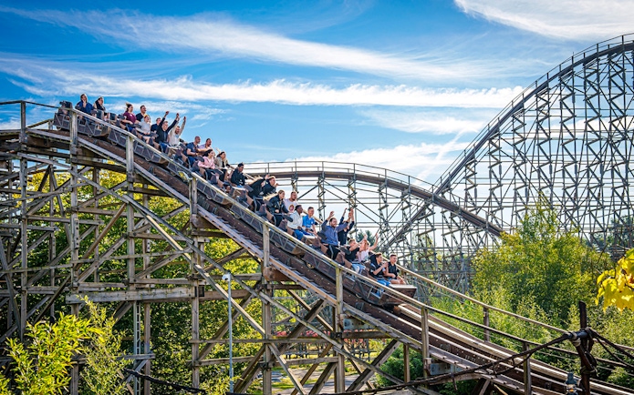 Roller coaster at Heide Park with riders descending a wooden track.
