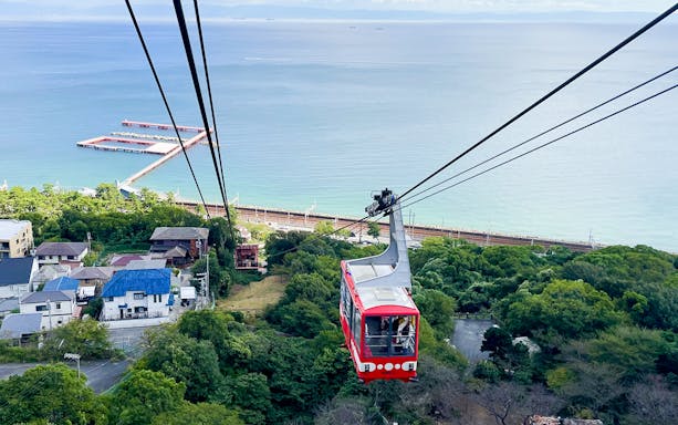 Cable car ascending over coastal town with ocean view in Japan.