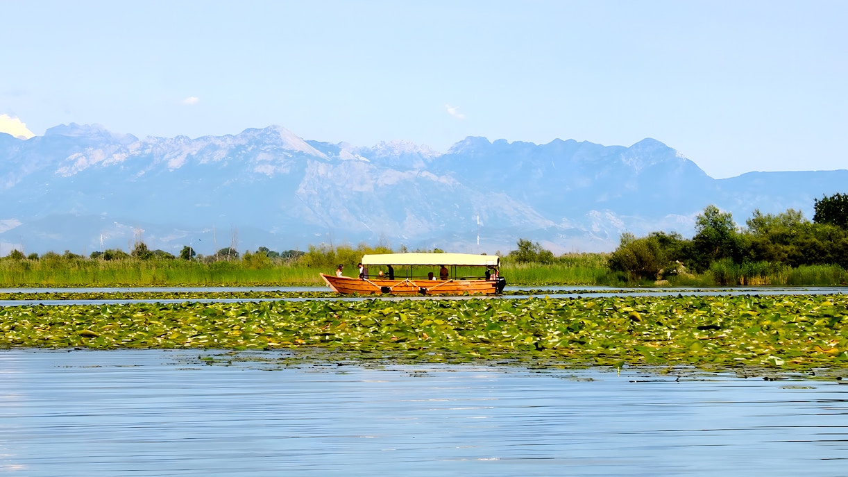 Wooden boat on Lake Skadar during guided sightseeing tour with mountain backdrop.